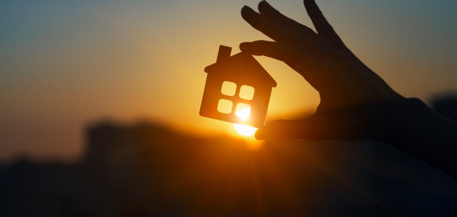 Man holding wooden house model against sunset light for sale or